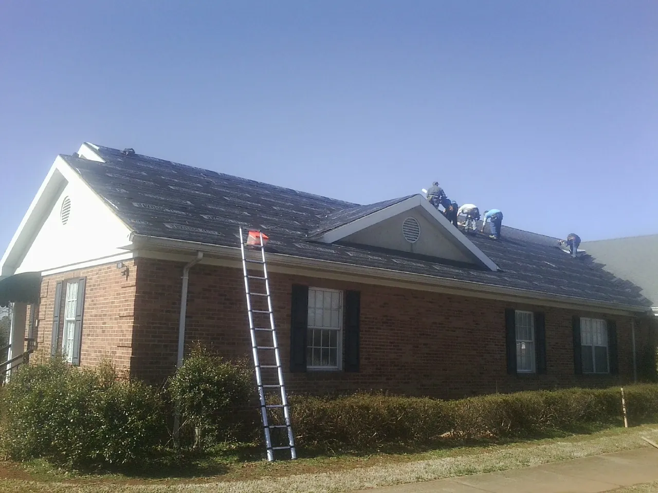 Crew tearing shingles off a brick ranch roof with a ladder set — Metal Roof Repair work by our crew in Hornsby