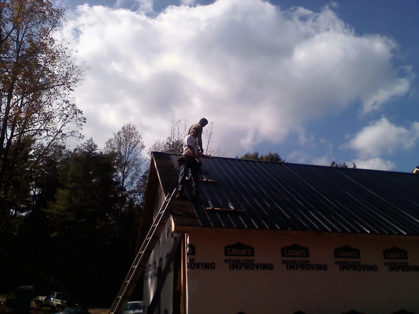 Roofer fastening dark metal panels high against a cloudy sky, from a Roof Inspection job in Hornsby
