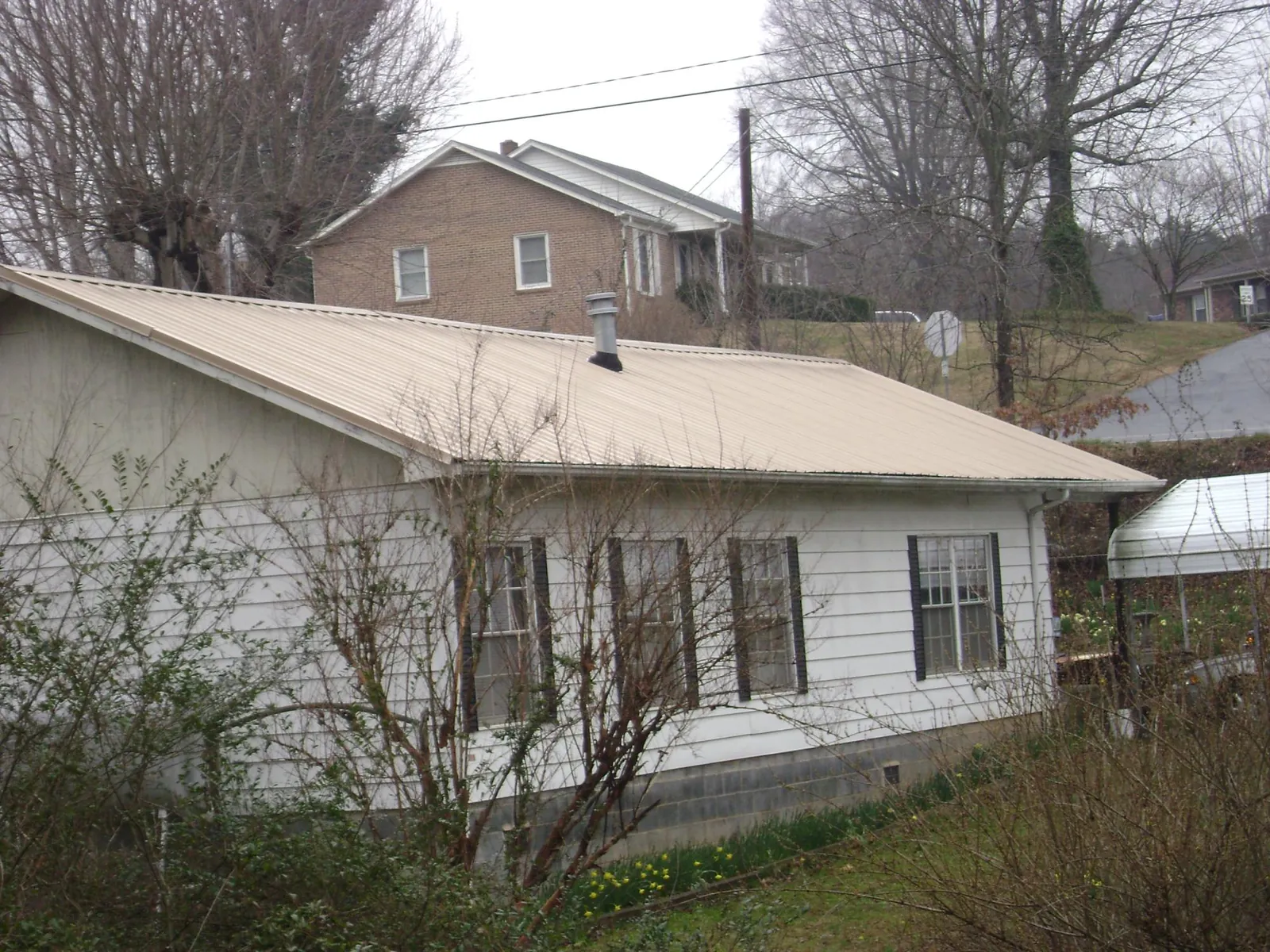Tan metal roof on a white sided house set into a hillside — Commercial Roofing by Roofing Brothers in Hornsby